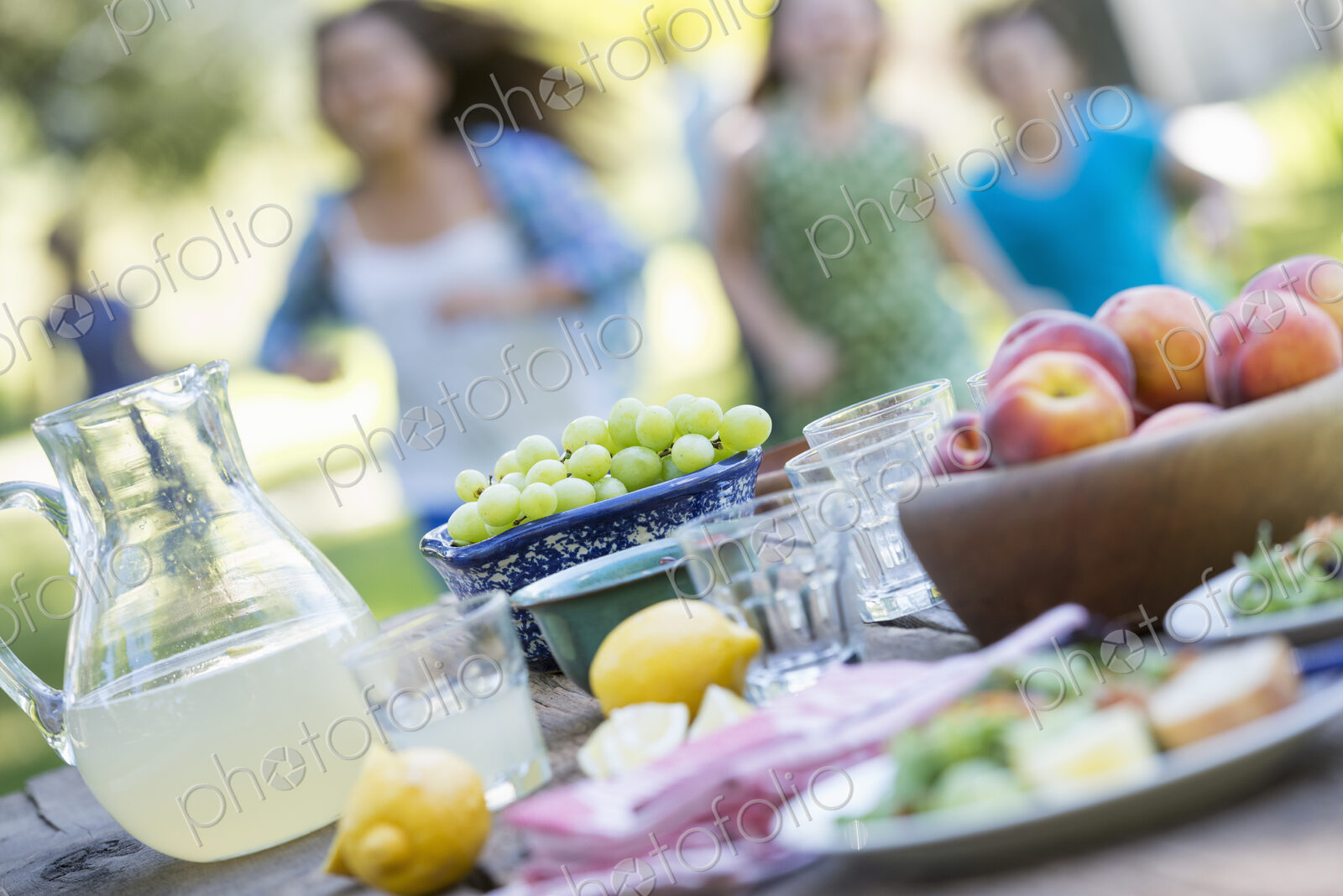 A summer buffet of fruits and vegetables, laid out on a table. Children running in the…