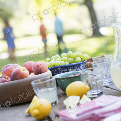 A summer buffet of fruits and vegetables, laid out on a table. People in the background.