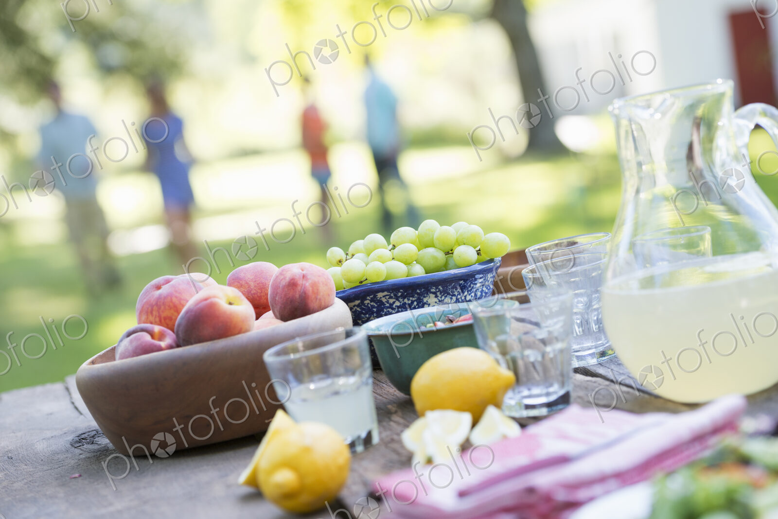 A summer buffet of fruits and vegetables, laid out on a table. People in the background.