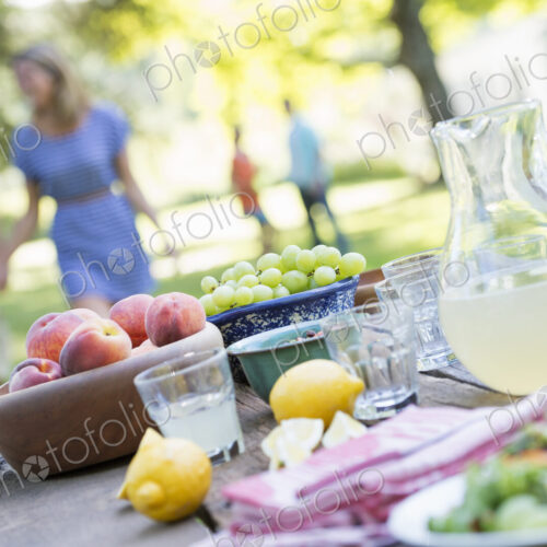 A summer buffet of fruits and vegetables, laid out on a table. People in the background.