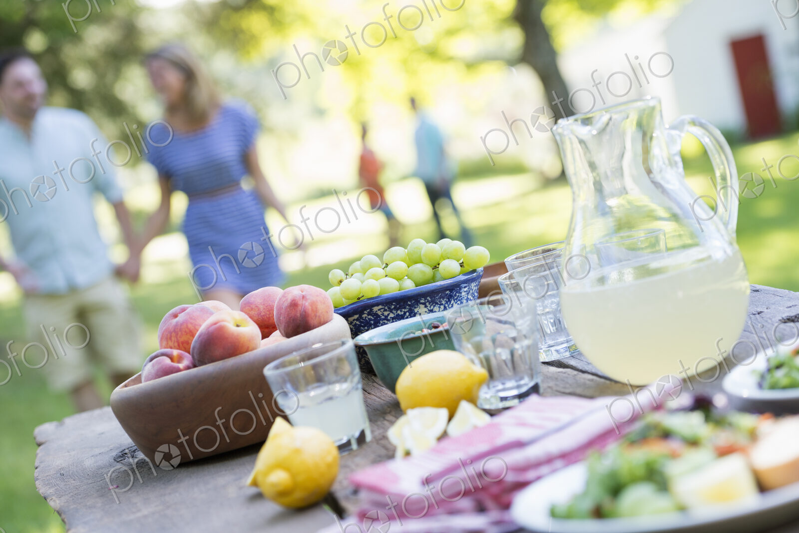 A summer buffet of fruits and vegetables, laid out on a table. People in the background.