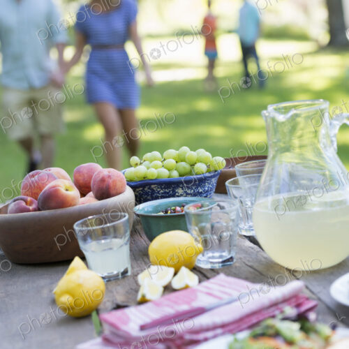 A summer buffet of fruits and vegetables, laid out on a table. People in the background.