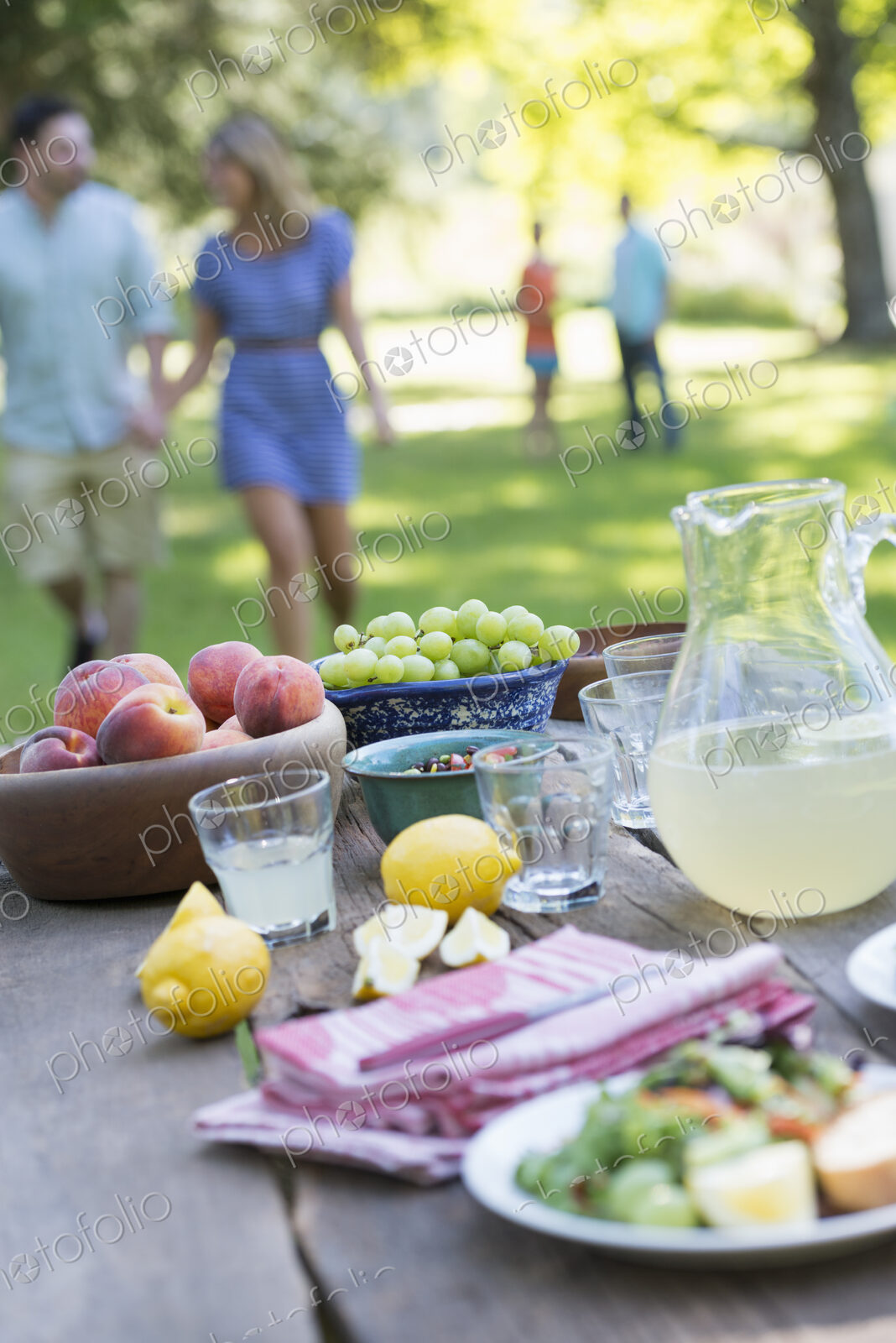 A summer buffet of fruits and vegetables, laid out on a table. People in the background.