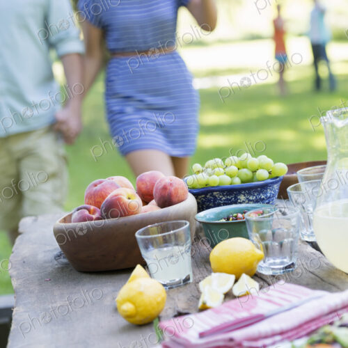 A summer buffet of fruits and vegetables, laid out on a table. People in the background.