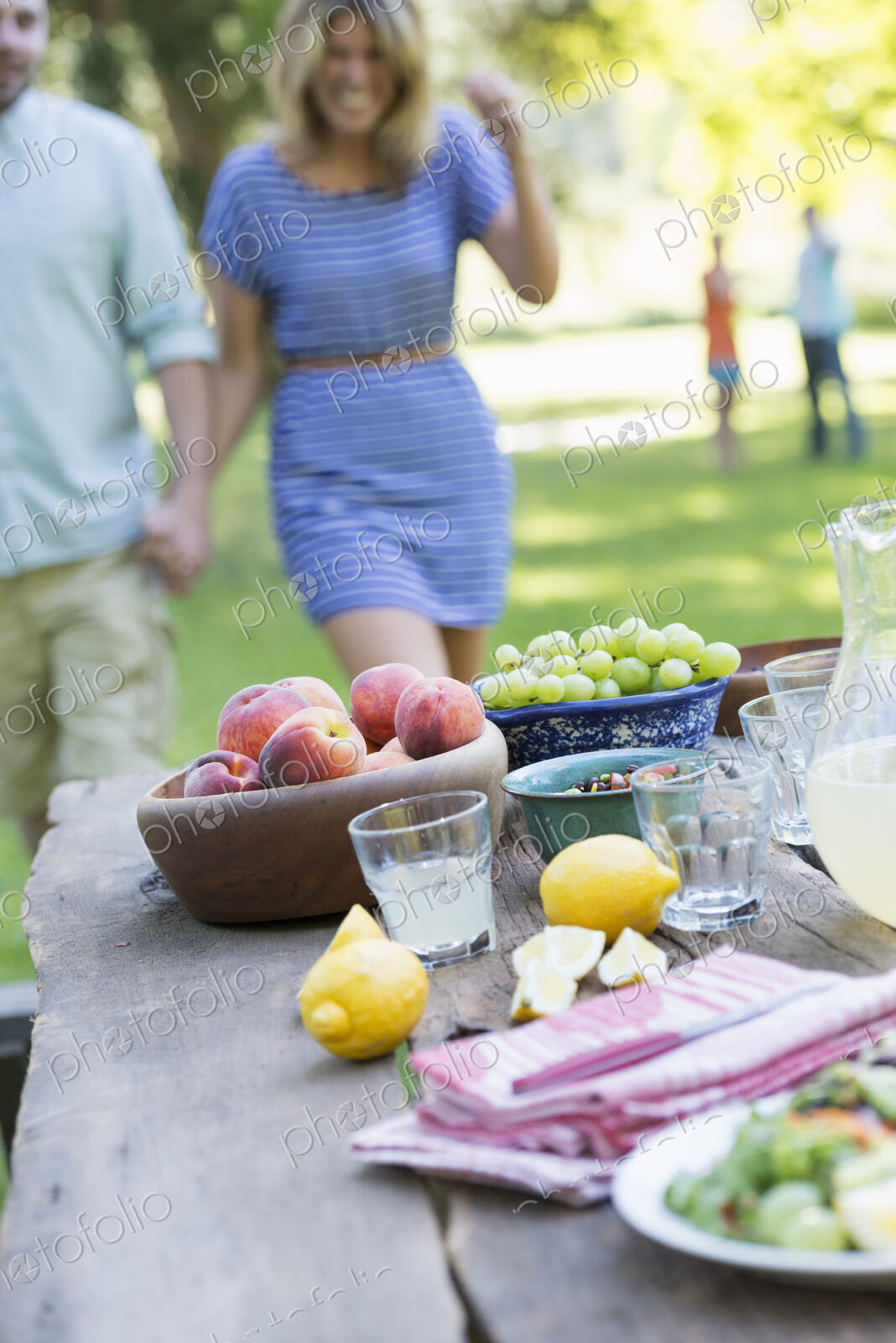 A summer buffet of fruits and vegetables, laid out on a table. People in the background.