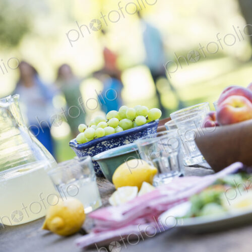 A summer buffet of fruits and vegetables, laid out on a table. People in the background.