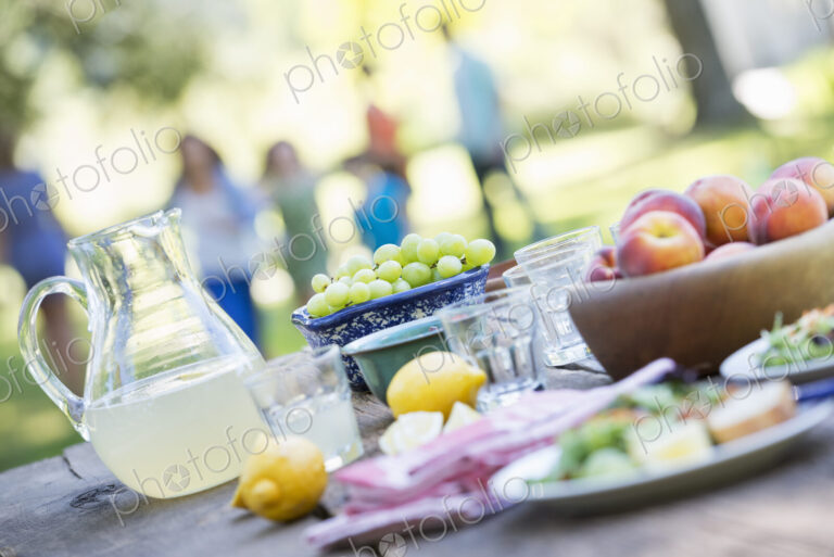 A summer buffet of fruits and vegetables, laid out on a table. People in the background.