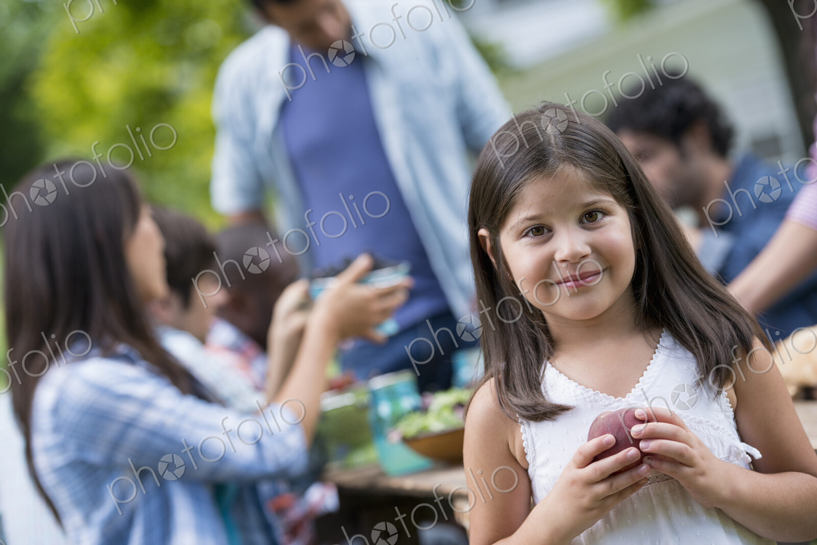 A summer party outdoors. Adults and children around a table.
