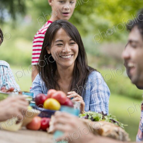 A summer party outdoors. Adults and children around a table.