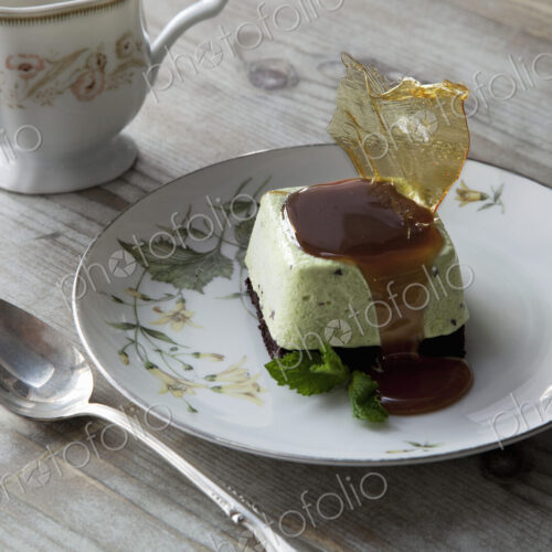 A sweet dessert dish with sugarwork and sauce on a china plate, with spoon and cup.