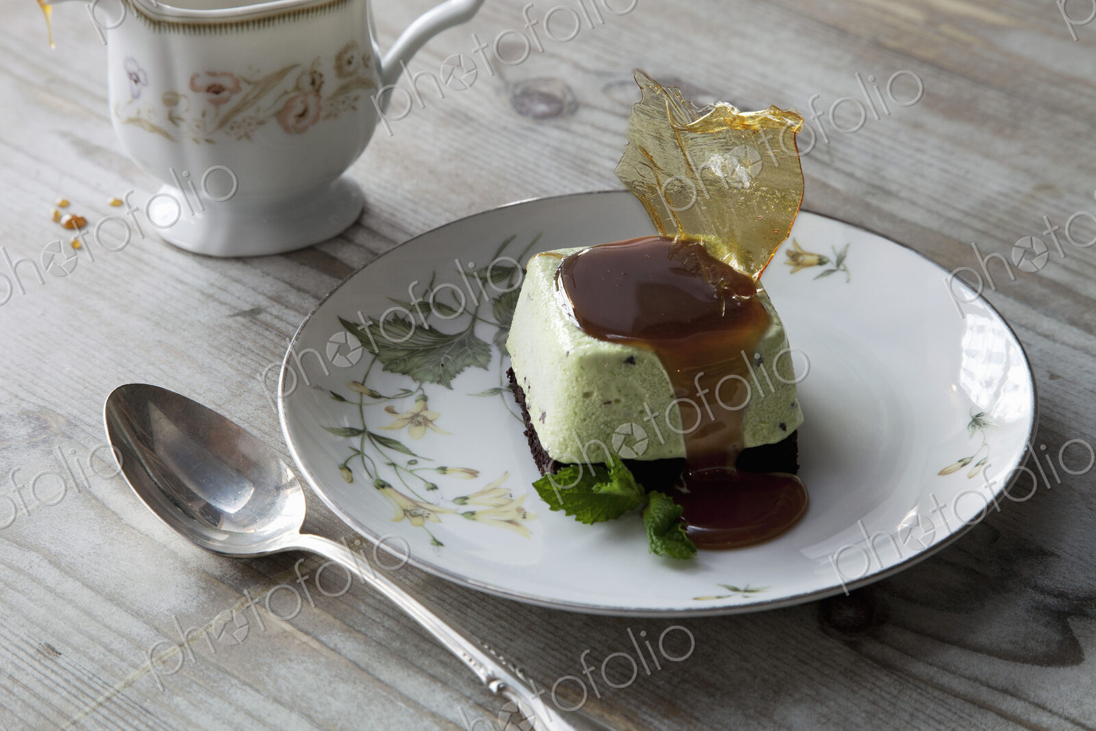 A sweet dessert dish with sugarwork and sauce on a china plate, with spoon and cup.