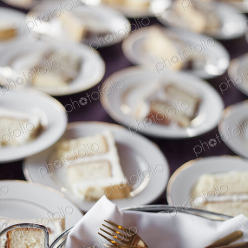 A table laden with plates. White china, and a basket full of dessert forks. A slice of… A table laden with plates. White china, and a basket full of dessert forks. A slice of…
