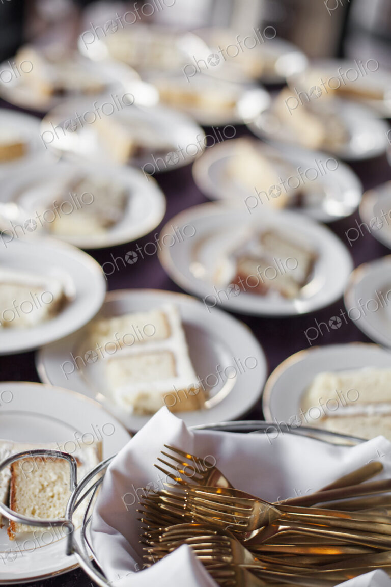 A table laden with plates. White china, and a basket full of dessert forks. A slice of…