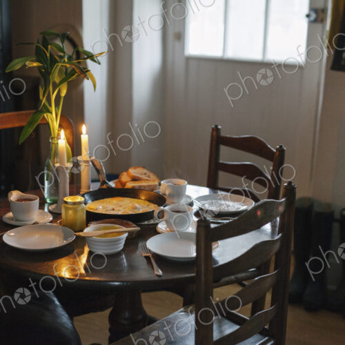 A table laid for a meal with lit candles, white crockery and a vase of flowers. A table laid for a meal with lit candles, white crockery and a vase of flowers.