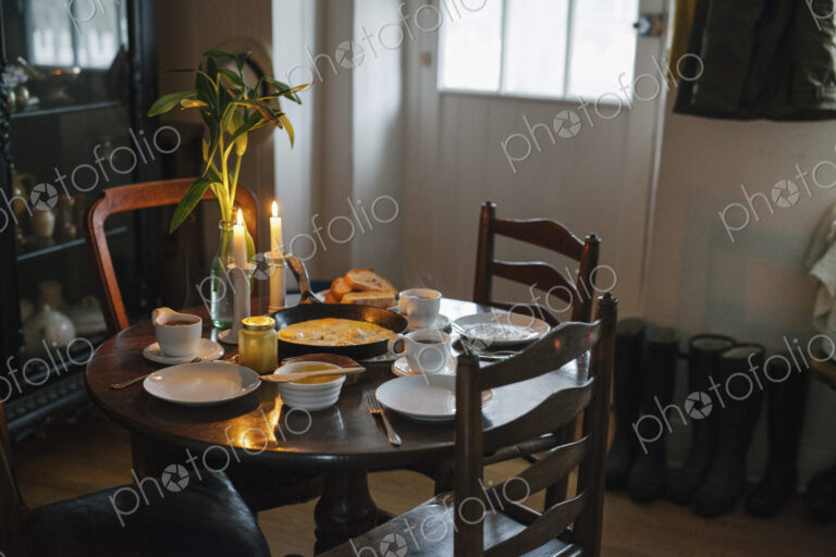 A table laid for a meal with lit candles, white crockery and a vase of flowers.