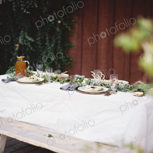 A table laid for a special meal. Place settings, with plates and cutlery. Glasses. A…
