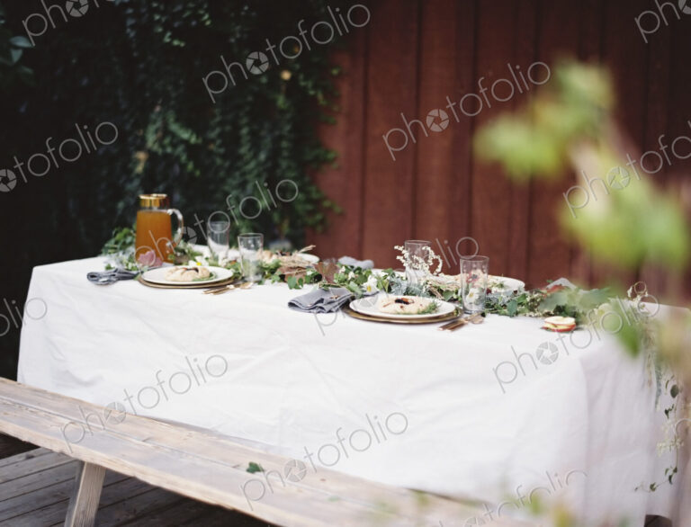 A table laid for a special meal. Place settings, with plates and cutlery. Glasses. A…