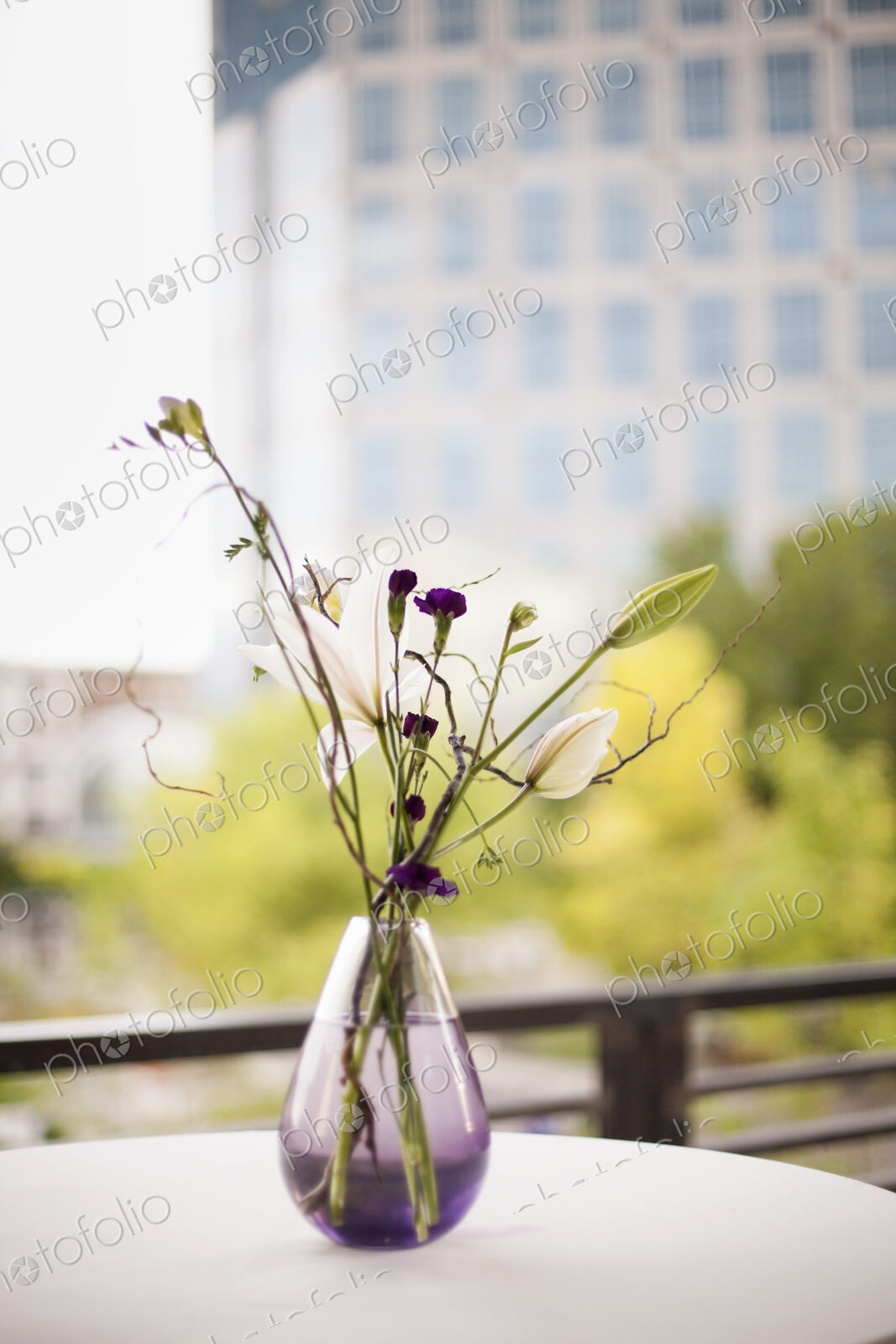 A table on a terrace in the city. A vase of flowers. Small purple flowers, and white…