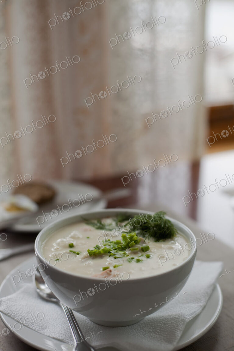 A table setting. A white china bowl of soup, with garnish. A table napkin. Wedding…