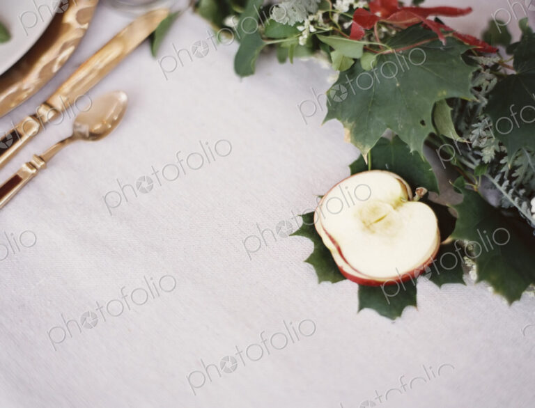 A table top covered with a white cloth. A place setting with cutlery and plate. An…