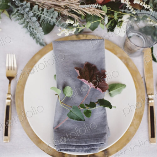 A table top covered with a white cloth. A place setting with cutlery and plate. A…