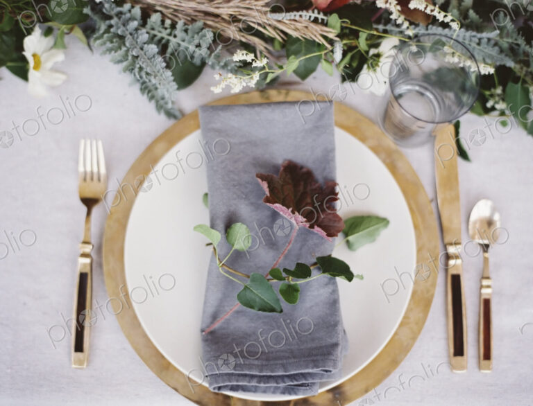 A table top covered with a white cloth. A place setting with cutlery and plate. A…