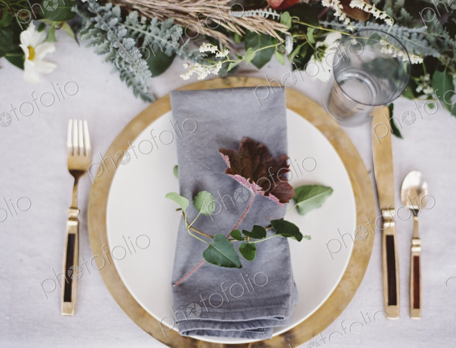 A table top covered with a white cloth. A place setting with cutlery and plate. A…