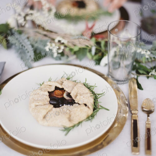 A table top covered with a white cloth. A place setting with cutlery and plate. A…