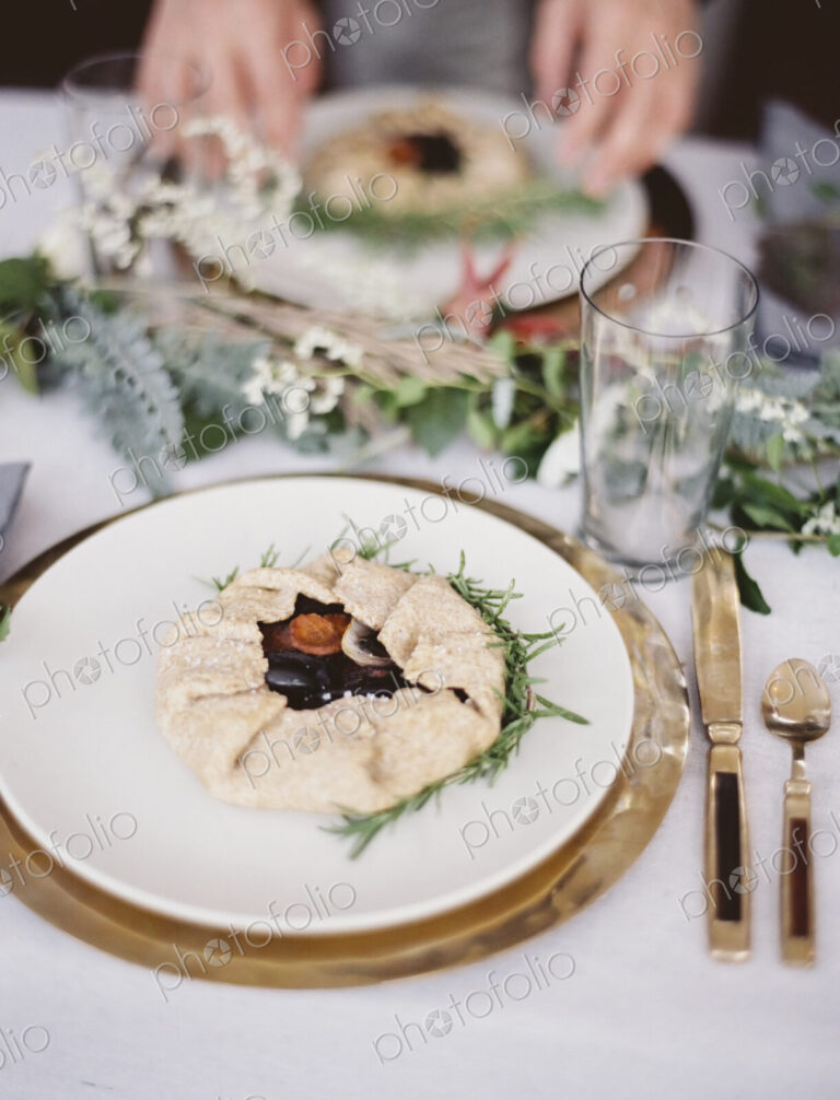A table top covered with a white cloth. A place setting with cutlery and plate. A…