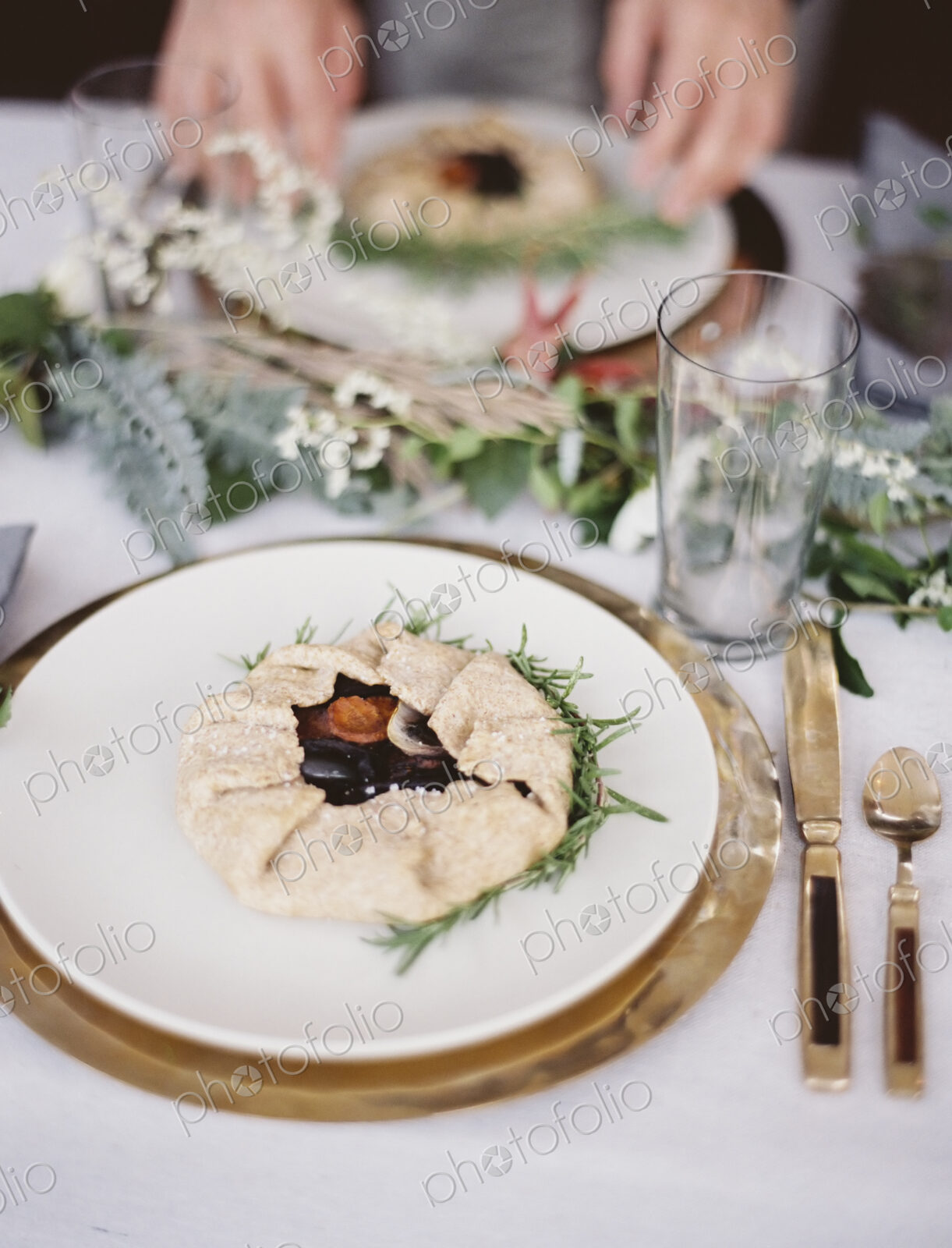 A table top covered with a white cloth. A place setting with cutlery and plate. A…