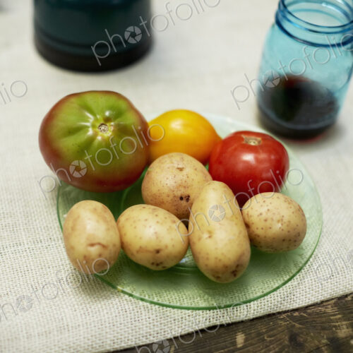 A table with a cloth, and plate with potatoes and tomatoes.