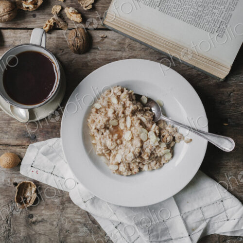 A table with a cup of coffee, bowl of muesli, nuts and an open book.
