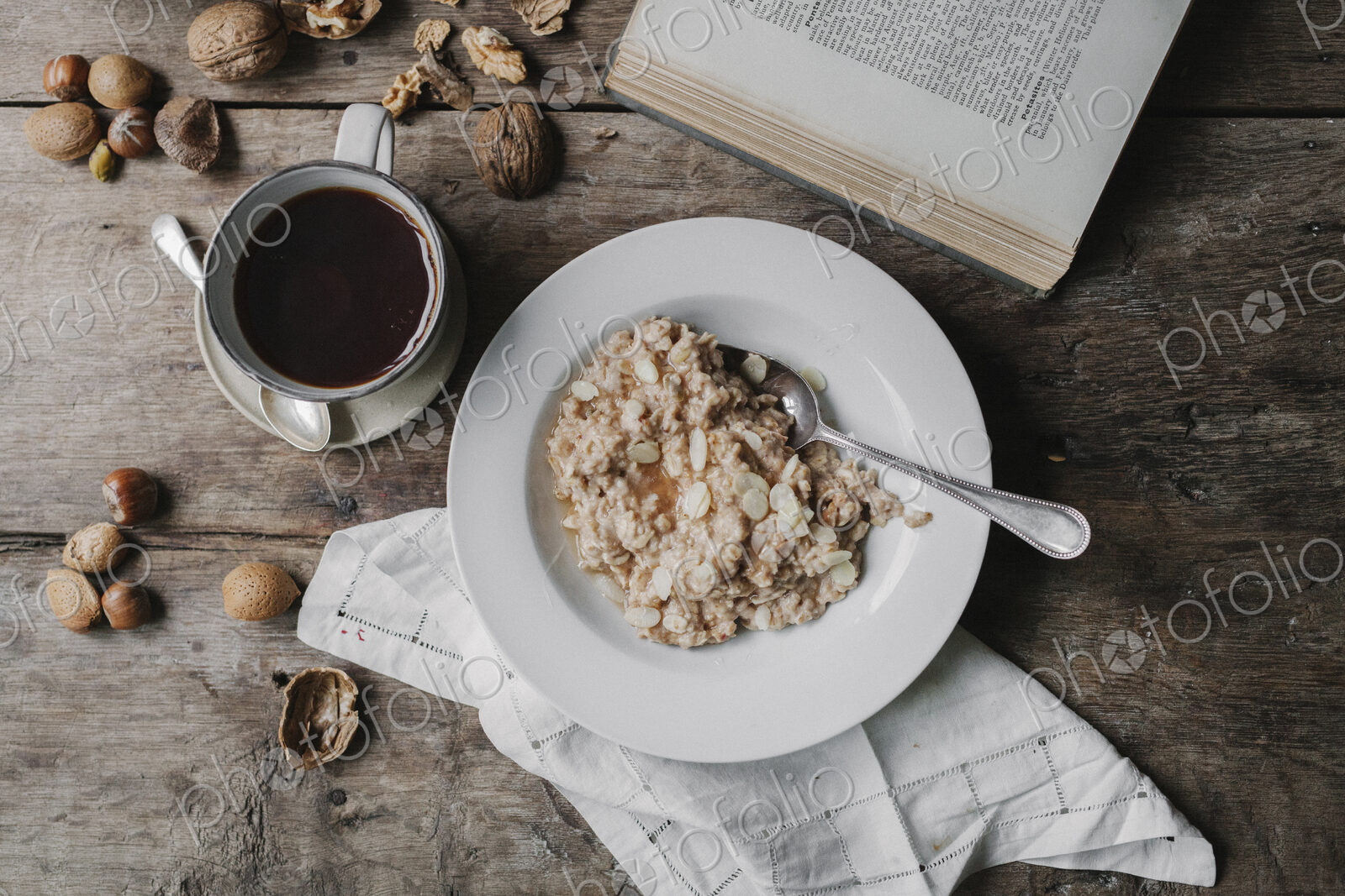 A table with a cup of coffee, bowl of muesli, nuts and an open book.