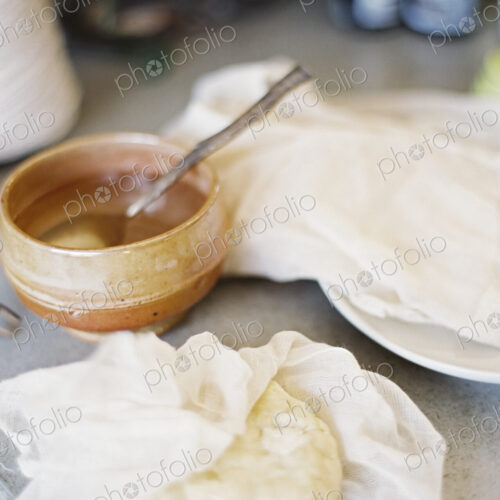 A tabletop in a domestic kitchen. A bowl of liquid with a spoon in it. A block of… A tabletop in a domestic kitchen. A bowl of liquid with a spoon in it. A block of…
