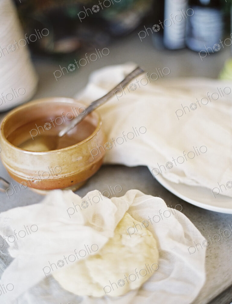 A tabletop in a domestic kitchen. A bowl of liquid with a spoon in it. A block of…