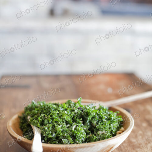 A tabletop with a log fire in the background. Green leafy salad in a wooden bowl. A tabletop with a log fire in the background. Green leafy salad in a wooden bowl.