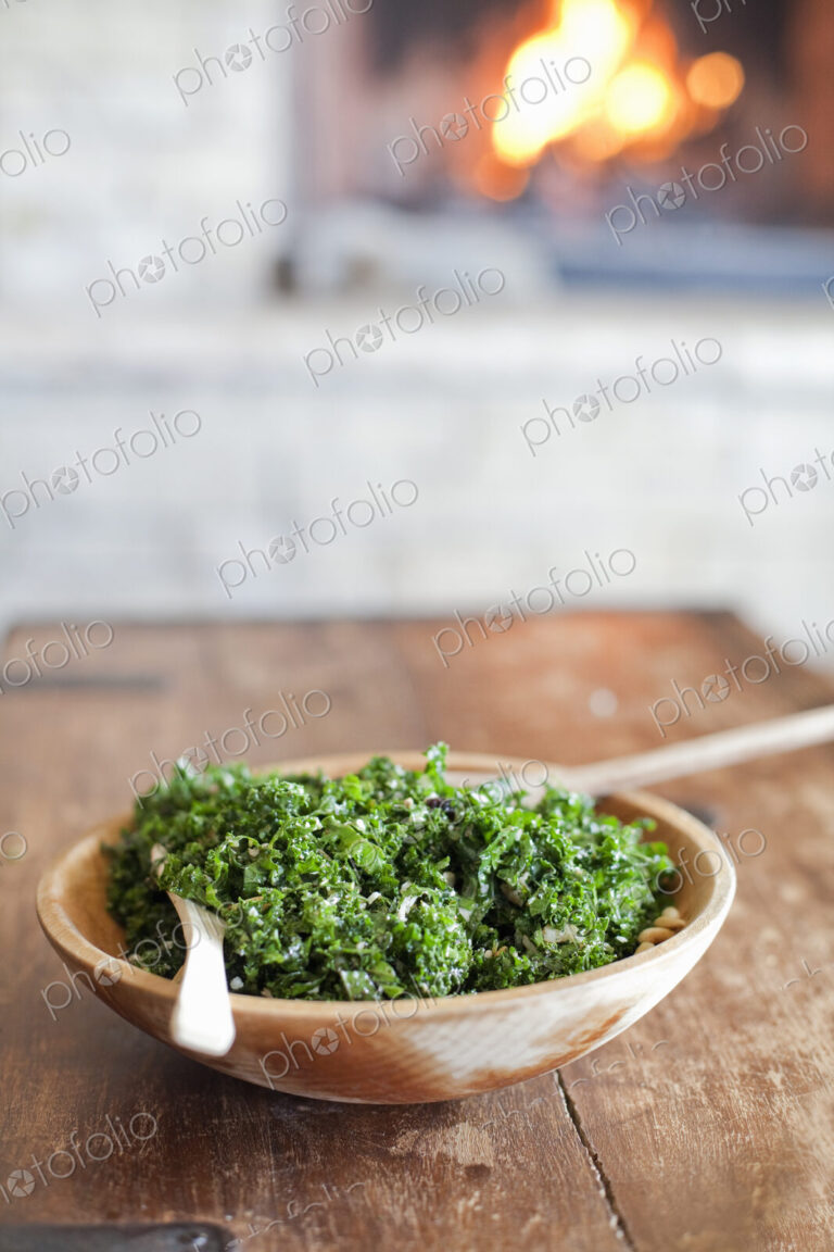 A tabletop with a log fire in the background. Green leafy salad in a wooden bowl.