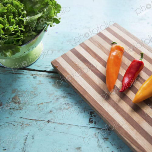 A tabletop with a wooden chopping board and three sweet peppers, and a bowl of salad… A tabletop with a wooden chopping board and three sweet peppers, and a bowl of salad…