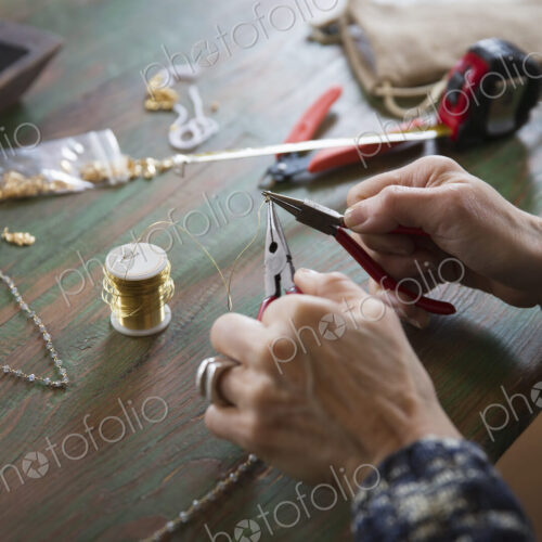 A tabletop with jewellery making equipment. Hands twisting wire on a necklace. A tabletop with jewellery making equipment. Hands twisting wire on a necklace.