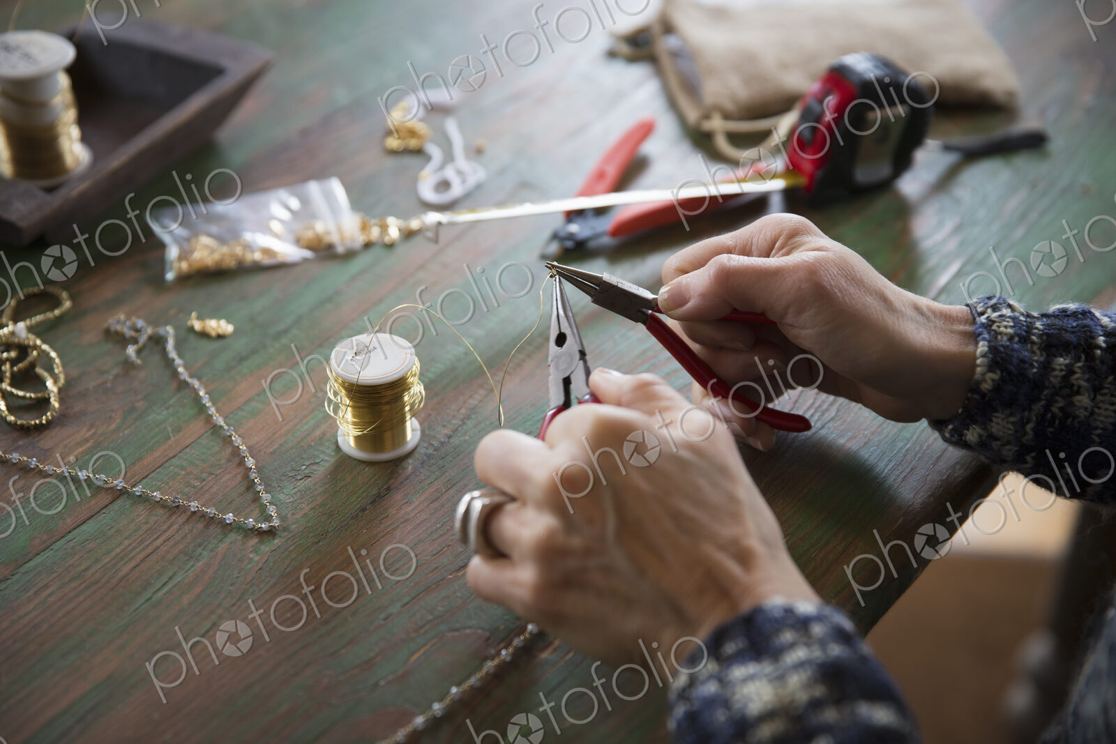 A tabletop with jewellery making equipment. Hands twisting wire on a necklace.