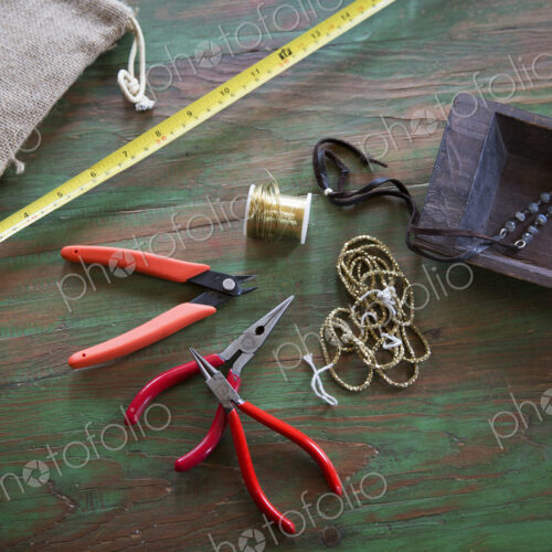 A tabletop with jewellery making equipment. Pliers, thread and a wooden tray, with…