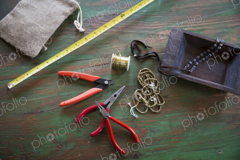 A tabletop with jewellery making equipment. Pliers, thread and a wooden tray, with…
