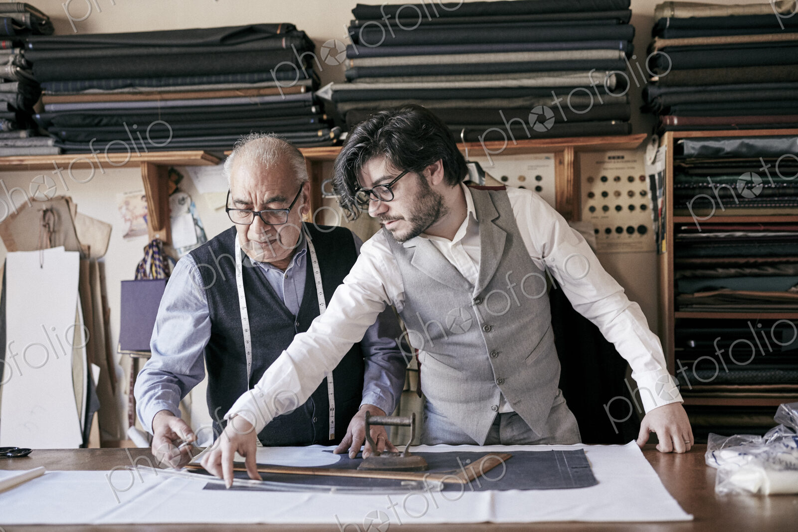 A tailor and a younger man, an assistant or apprentice working together, measuring…