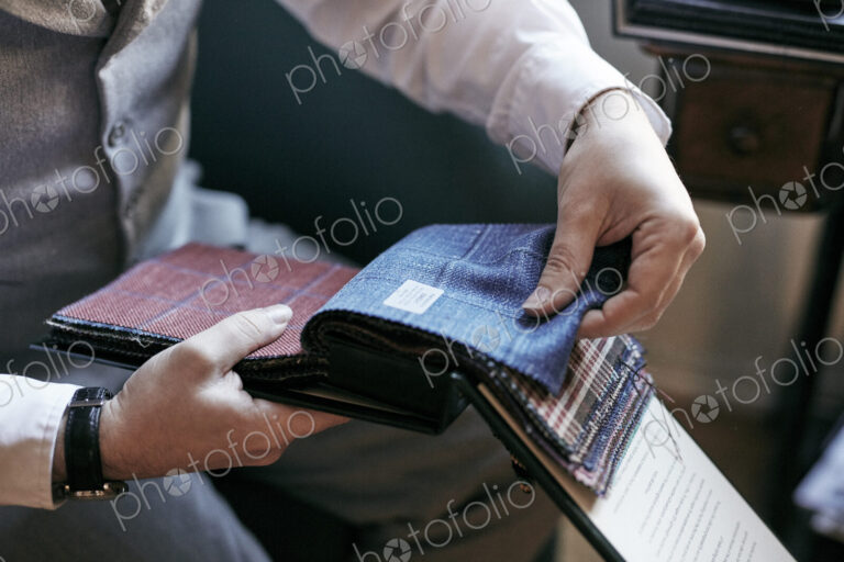 A tailor looking at fabric samples in a book, tweed and wool for mens clothes.
