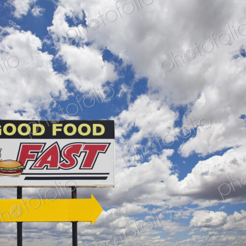A tall Good Food Fast sign on a desert road with a bright yellow arrow. A tall Good Food Fast sign on a desert road with a bright yellow arrow.