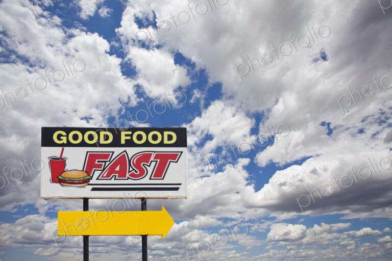 A tall Good Food Fast sign on a desert road with a bright yellow arrow.