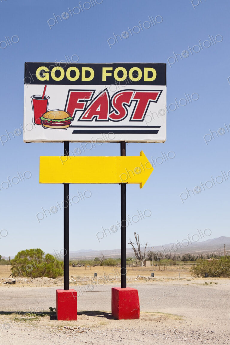 A tall Good Food Fast sign on a desert road with a bright yellow arrow.