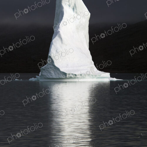 A tall pillar of ice, the top of an iceberg lit up floating on the sea, reflected in… A tall pillar of ice, the top of an iceberg lit up floating on the sea, reflected in…