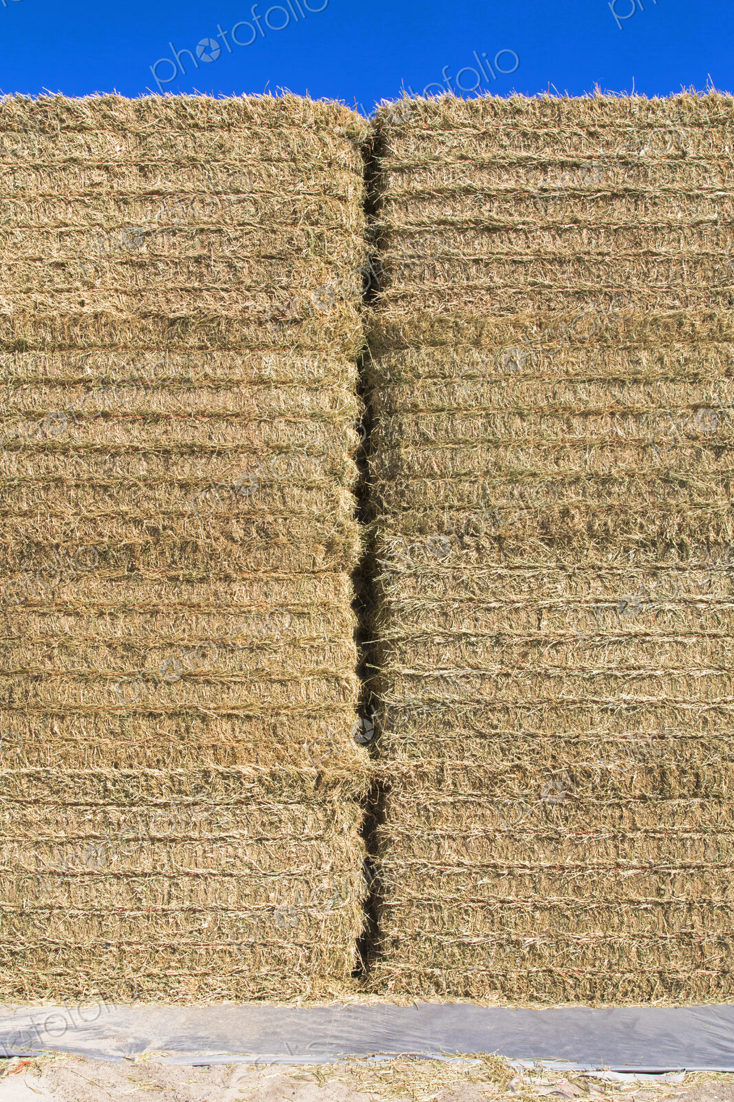 A tall stack of hay bales in a farmyard. Neatly packed and baled.