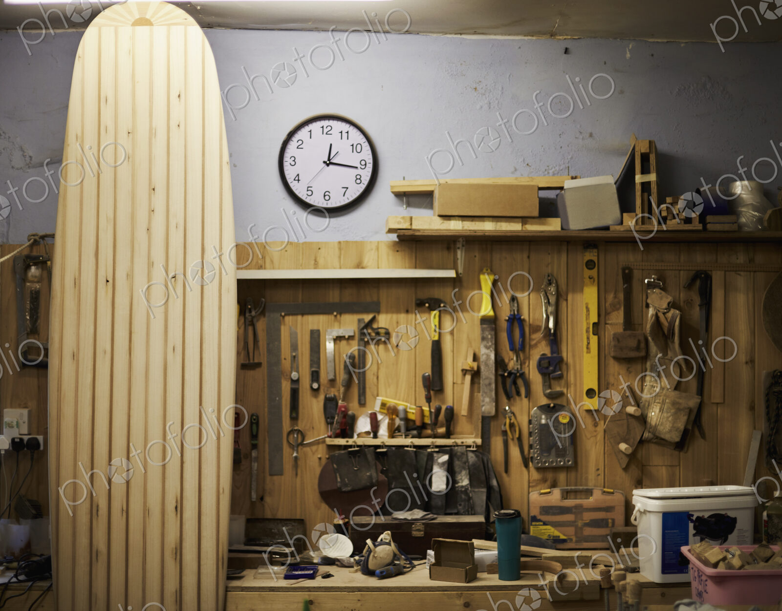 A tall wooden surfboard propped up in a workshop.